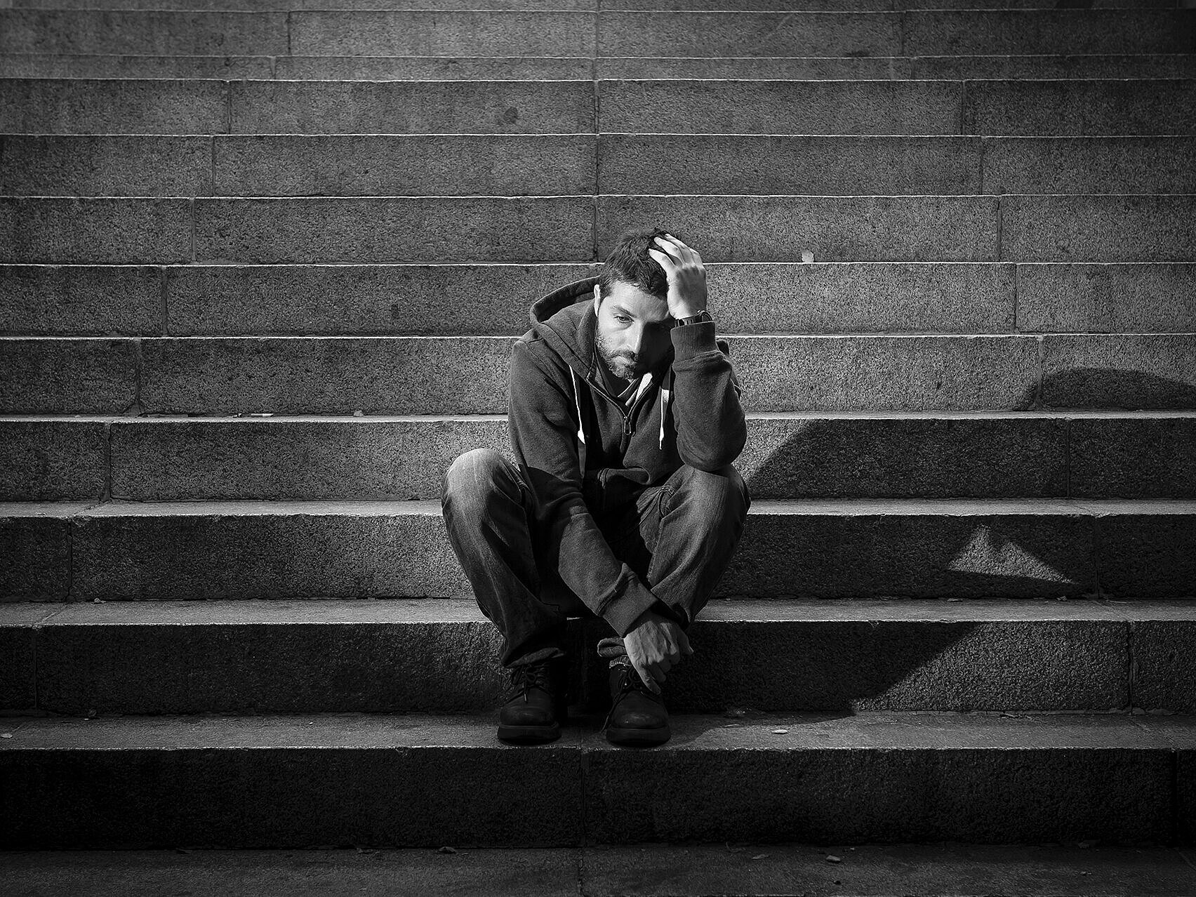 Bild: Junger Mann sitzt niedergeschlagen auf einer Treppe