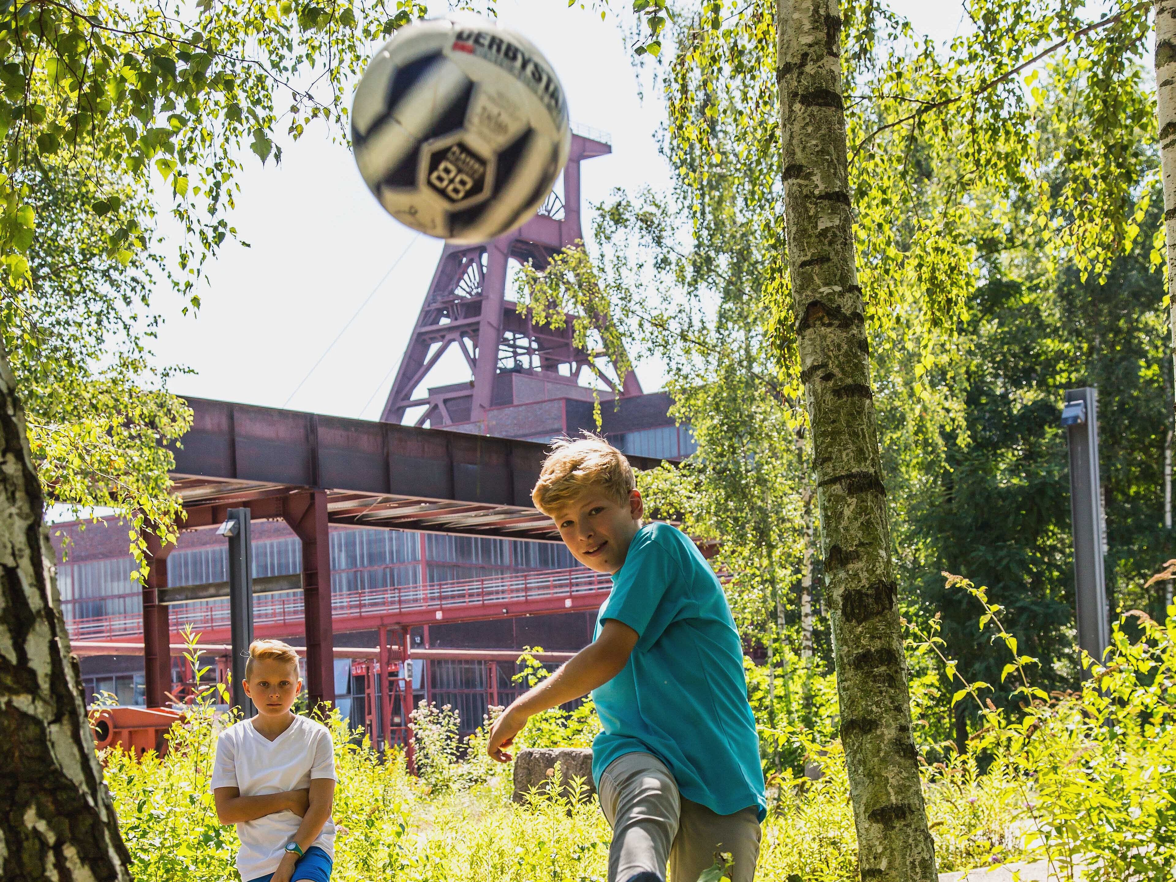 Bild: Zwei fußballspielende Jungs im Hintergrund der Förderturm der Zeche Zollverein